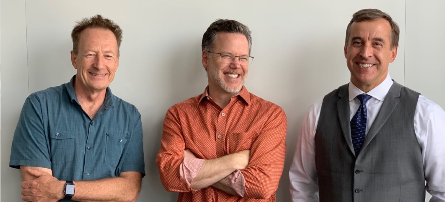 three men laughing and smiling, leaning on a wall