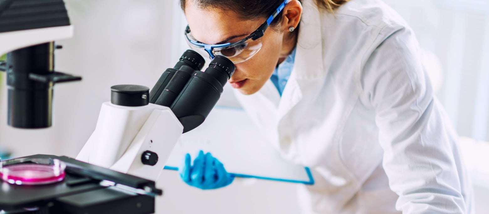 stock photo, woman in lab coat and gloves, looking in a microscope